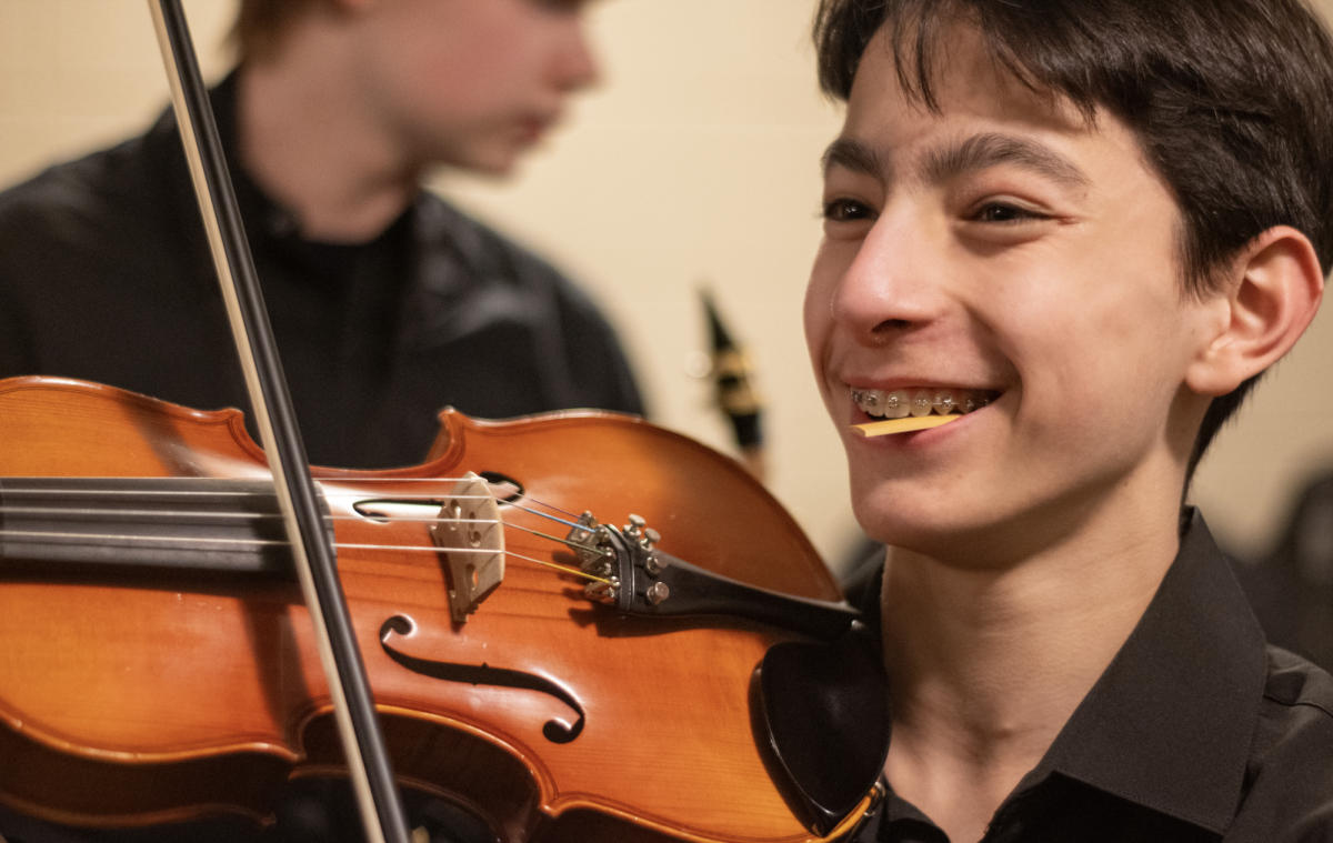 Before the Dec. 18 high school music concert at Mandel Hall, ninth grader Ari Wong prepares by wetting the reed for his clarinet while laughing and playing around with a friend's violin.